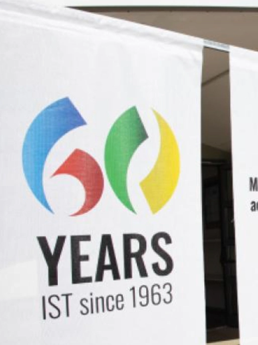 Pannello bianco con scritta “60 years IST since 1963”. La cifra sei è formata da due pennellate, una azzurra e una rossa, lo zero da una verde e una gialla