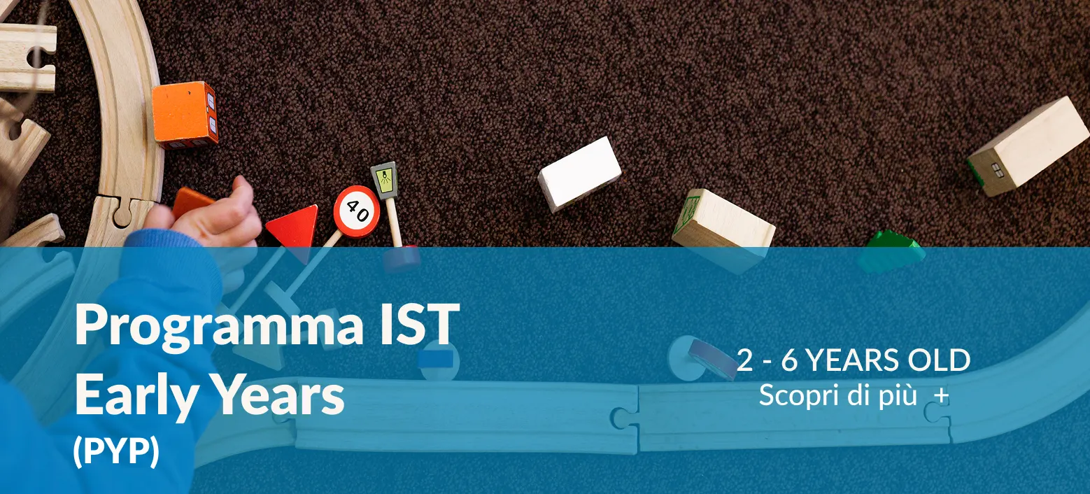 Foto di una moquette marrone con parti di un trenino in legno. La parte inferiore è parzialmente coperta da una banda azzurra con la scritta “Programma Primary Years (PYP)” che rimanda alla pagina omonima