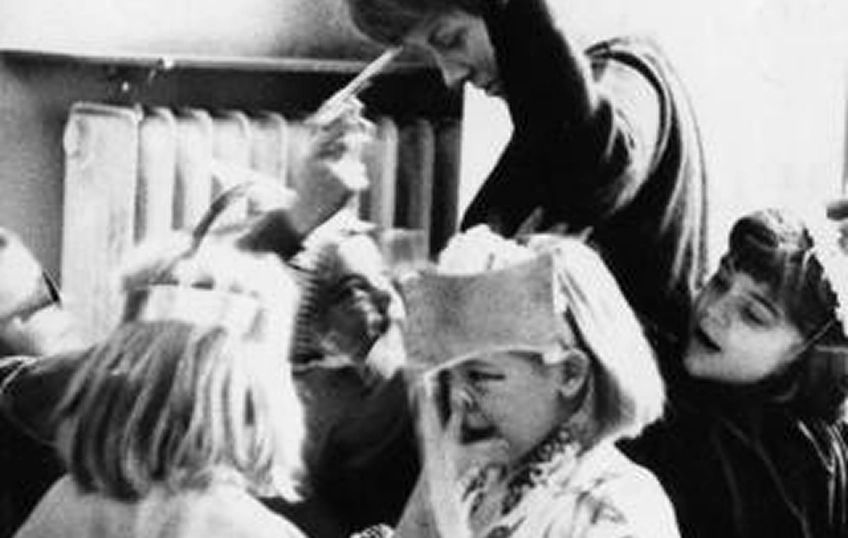 Immagine in bianco e nero, di cinque bambini mascherati e un’adulta con le braccia alzate