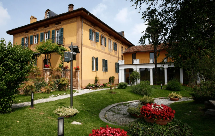 Immagine della sede di IST, con il campus, zona verde con prato all’inglese e aiuole fiorite rosse e bianche. Sullo sfondo il corpo della scuola e il porticato bianco