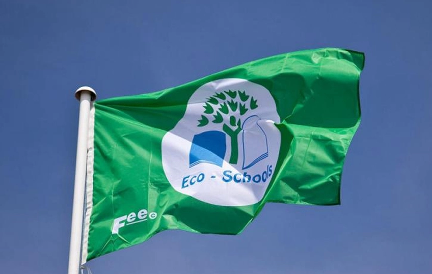 Bandiera verde con la scritta “Eco-School” in un cerchio centrale bianco con un albero verde, sventola sullo sfondo di un cielo senza nubi