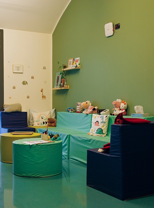 Locale dedicato al counselling, uno dei servizi scolastici proposti da IST. Il pavimento e una parete sono verdi, sono presenti poltroncine e pouf blu, gialli e verdi, giocattoli e libri