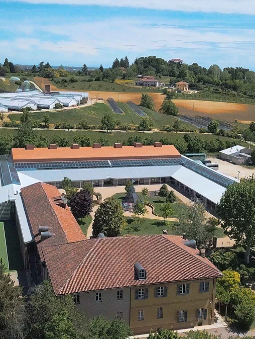 Panoramica dell’IST campus Torino, circondato da campi. Edificio giallo con tetto in tegole, unito a una costruzione a U di colore grigio, con area giochi