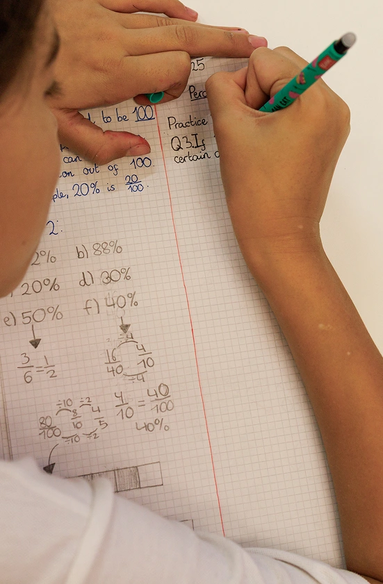 Una scolara scrive con una penna su un foglio a quadretti nell’ambito dei servizi di supporto scolastico dell’IST