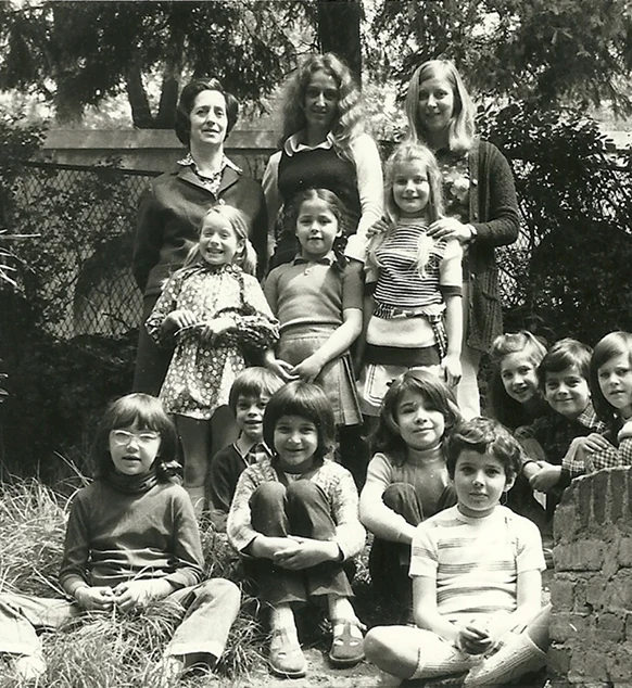 Fotografia in bianco e nero, risalente agli anni ’60 del secolo scorso, di insegnanti e bambini nel giardino di IST: quelli in prima fila sono seduti a terra, gli altri sono in piedi, sullo sfondo una recinzione