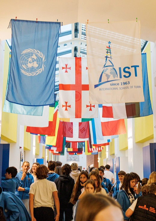 Insieme di vessilli dell’IST, dell’ONU e di numerose nazioni che sono appesi nella galleria dell’IST, sopra una moltitudine colorata di studenti che indossano la divisa della scuola