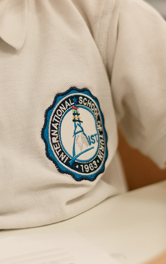 Particolare di una polo bianca con il logo circolare IST, indossata da uno studente del baccalaureato internazionale. Al centro la Mole Antonelliana stilizzata in azzurro con righe orizzontali colorate