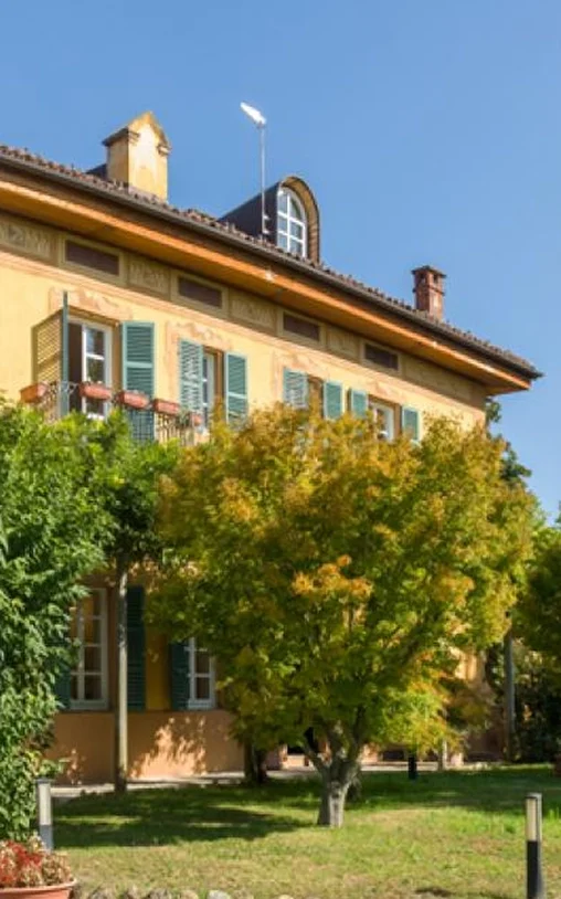 Foto dell’ala antica dell’International School of Turin (IST): villa ottocentesca a due piani di colore arancio con tetto in tegole rosse. Davanti alla costruzione un prato curato con alberi